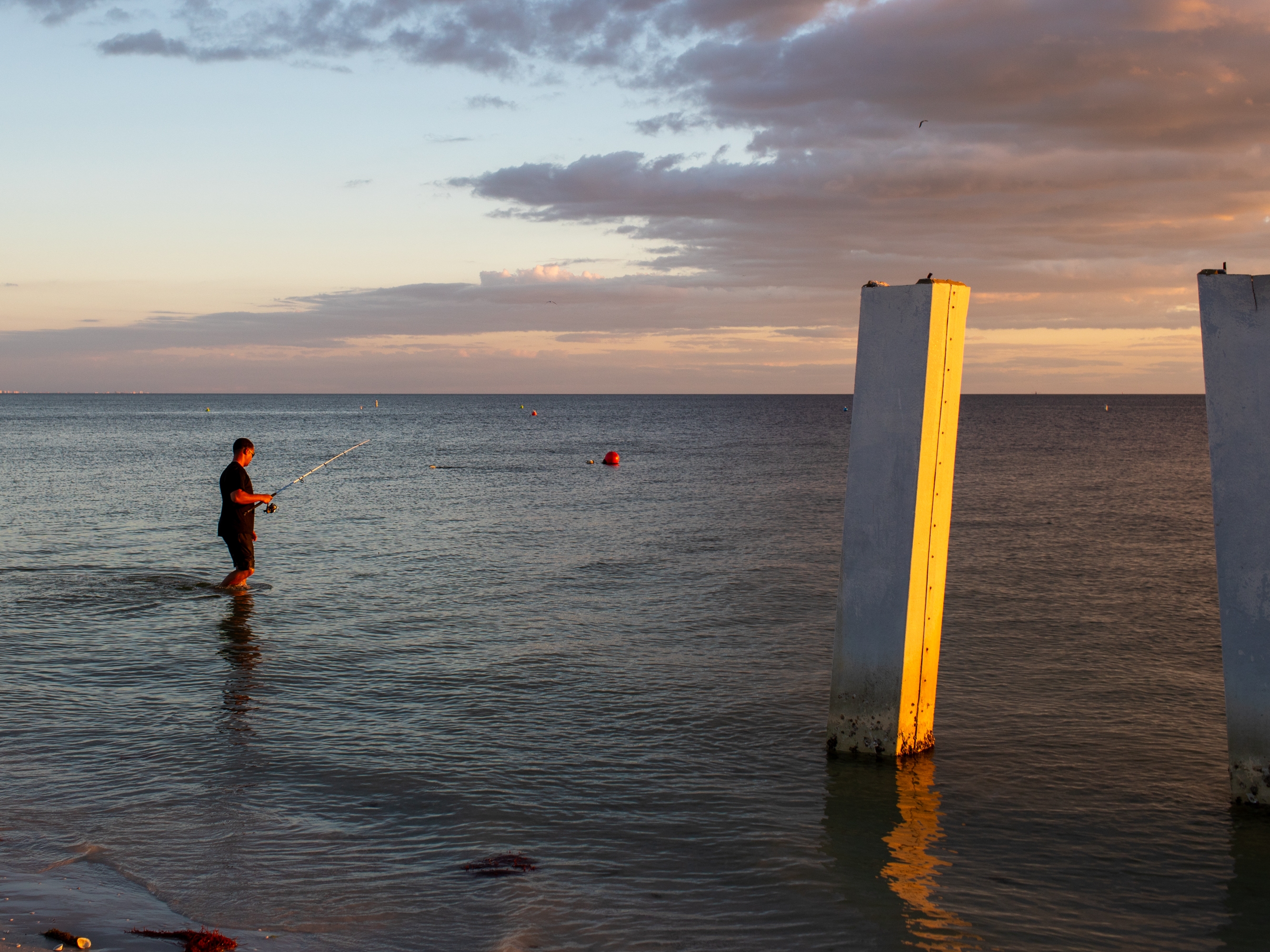 caption: A person fishes next to a broken pier in Fort Myers Beach, Fla., in October. The city is still rebuilding after Hurricane Ian devastated the area in 2022. High costs for construction and insurance have made Fort Myers Beach unaffordable for many who called it home before.