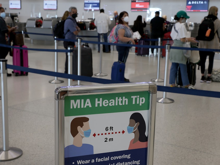 caption: A sign advises people to wear a mask and stand six feet apart as travelers make their way through Miami International Airport in December 2021 in Miami. A federal judge in Florida has ruled that the federal mask mandate on planes, trains, buses and other modes of public transportation is unlawful.