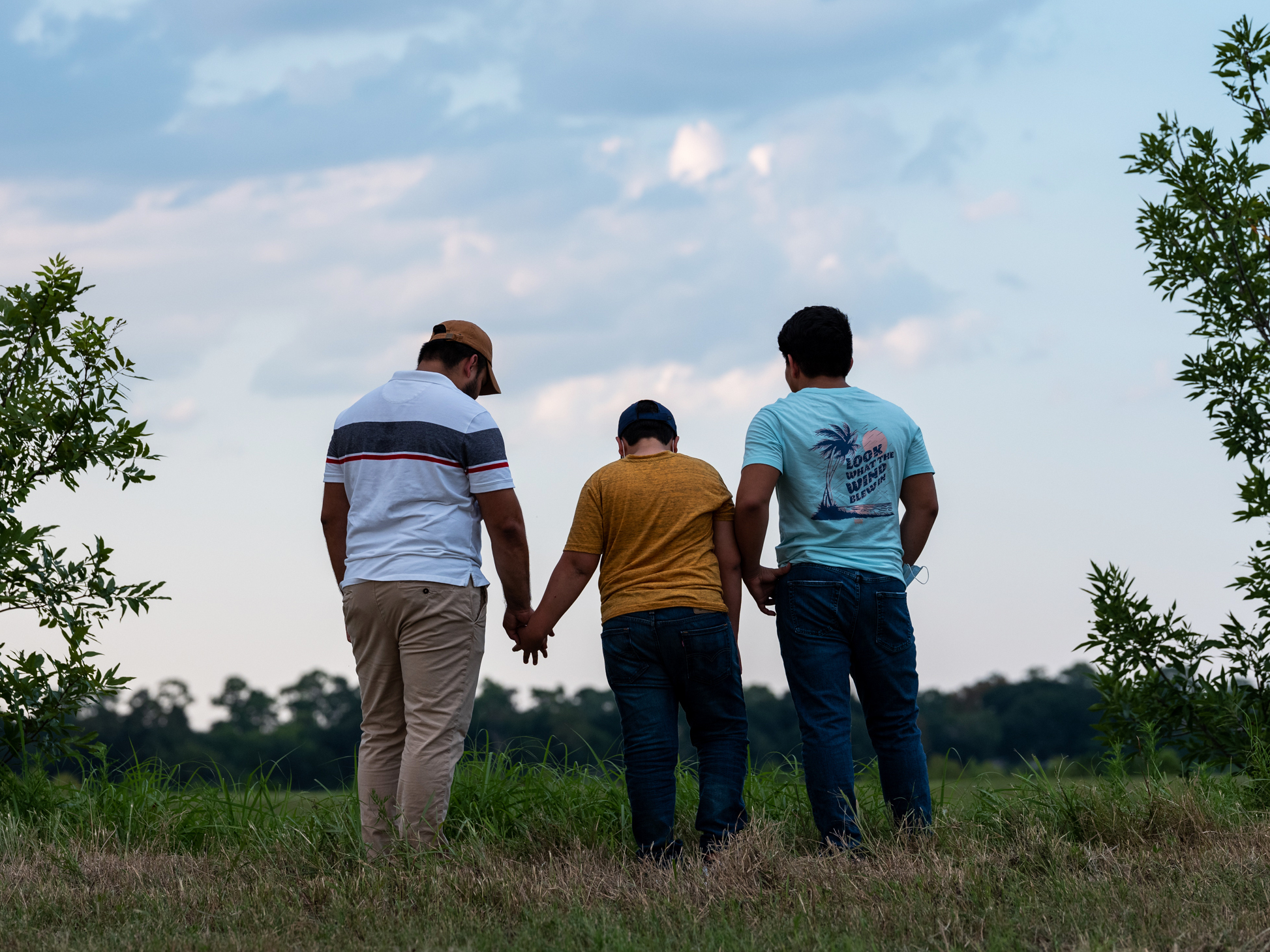 caption: Honduran migrants, Ricardo Sr., (left), his son Ricardo Jr., 13, and his cousin Jorge, 16, walk near their home in Texas. When the two teenage boys crossed the border illegally into Texas last month, they turned themselves into Border Patrol. They were later escorted to a hotel by armed men in civilian clothes.