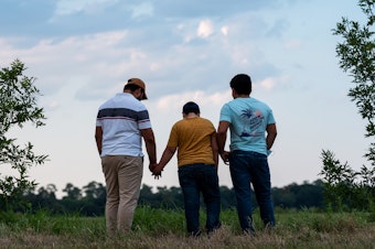 caption: Honduran migrants, Ricardo Sr., (left), his son Ricardo Jr., 13, and his cousin Jorge, 16, walk near their home in Texas. When the two teenage boys crossed the border illegally into Texas last month, they turned themselves into Border Patrol. They were later escorted to a hotel by armed men in civilian clothes.