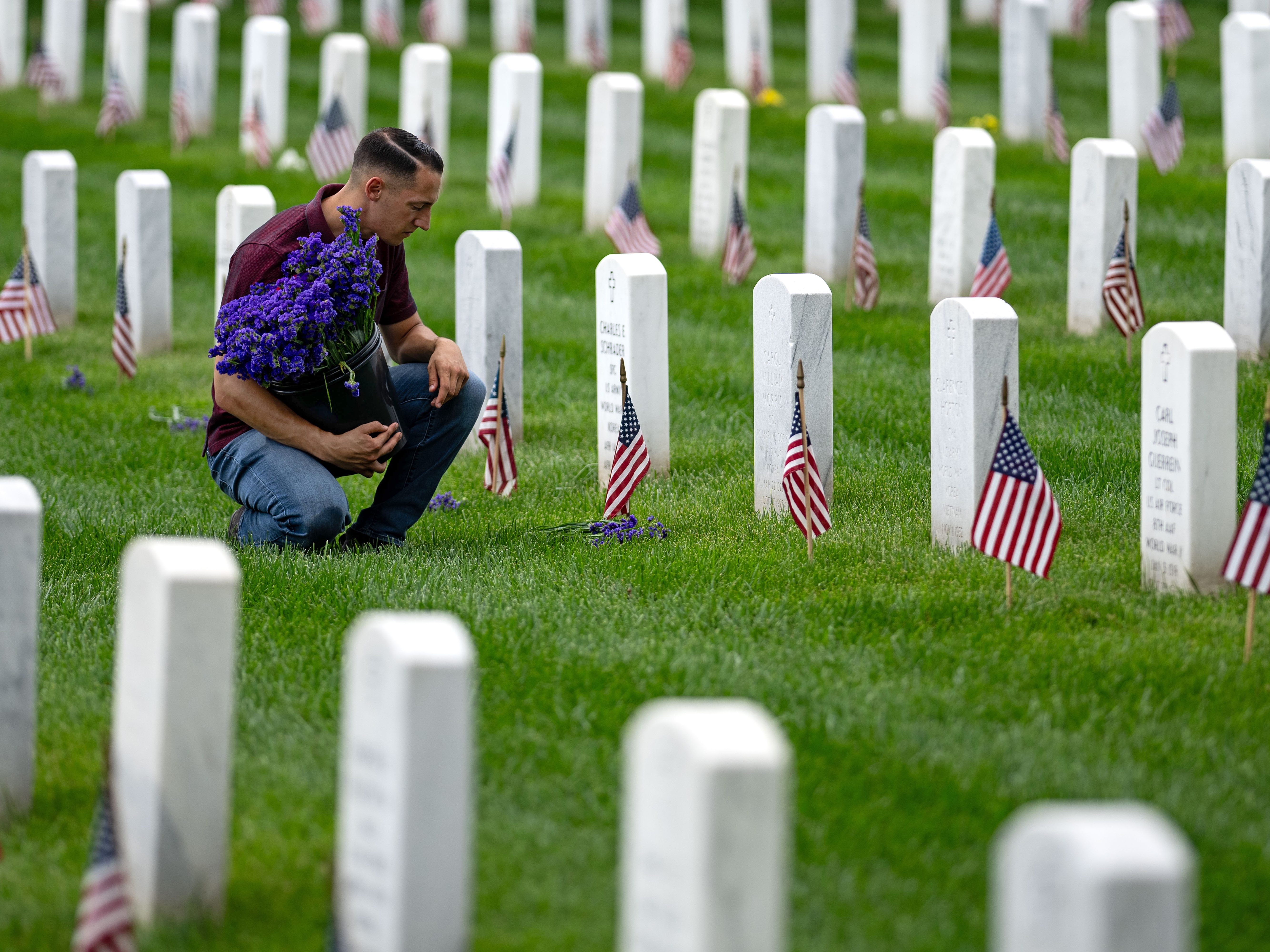 caption: A man places flowers in front of headstones in Section 60, which mark the final resting place of service men and women at Arlington National Cemetery on May 27 in Arlington, Va.