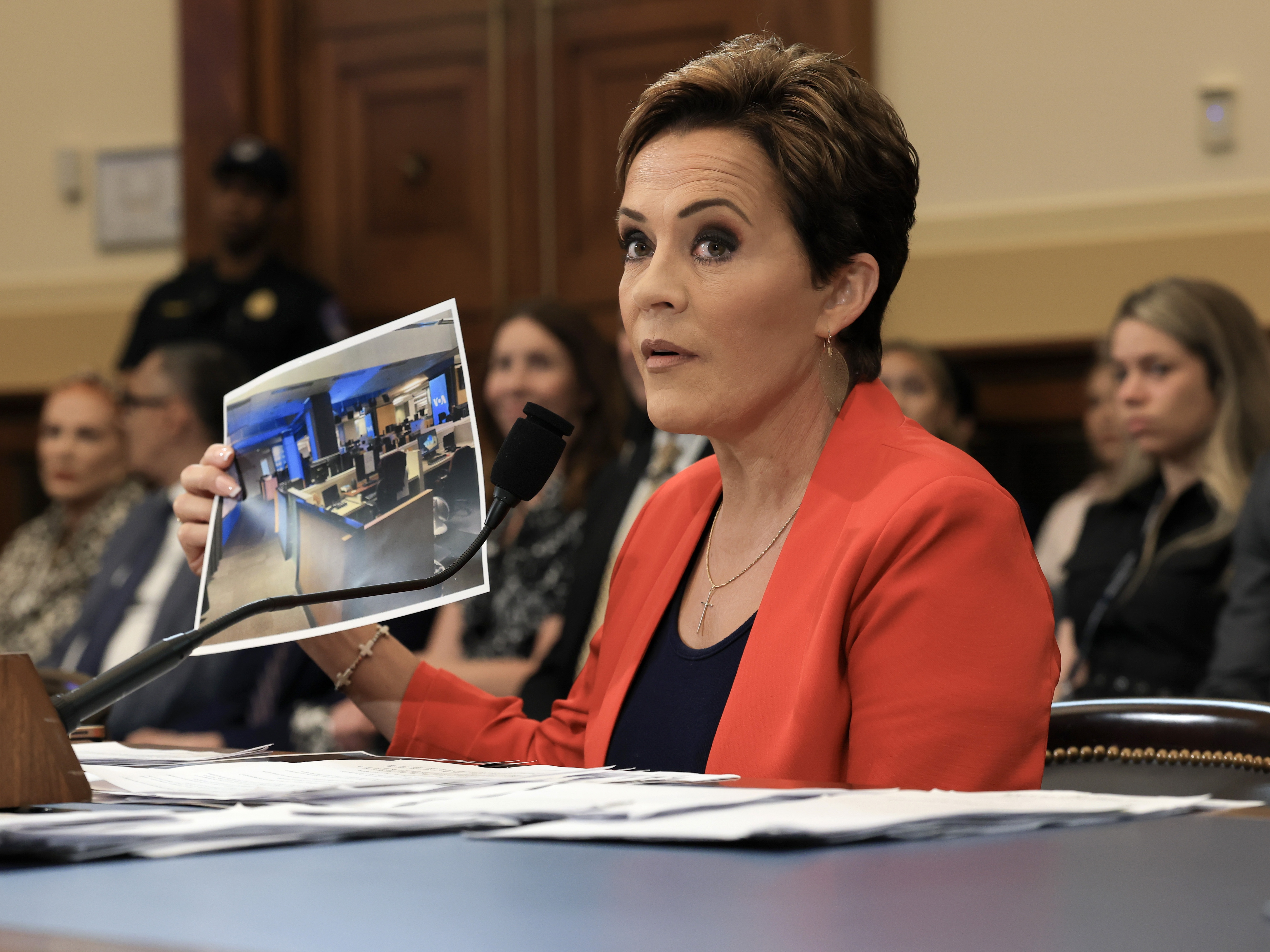 caption: Trump adviser Kari Lake holds up a photograph, which she says shows an empty Voice of America (VOA) newsroom, as she speaks during a U.S. House Committee on Foreign Affairs hearing on June 25, 2025.