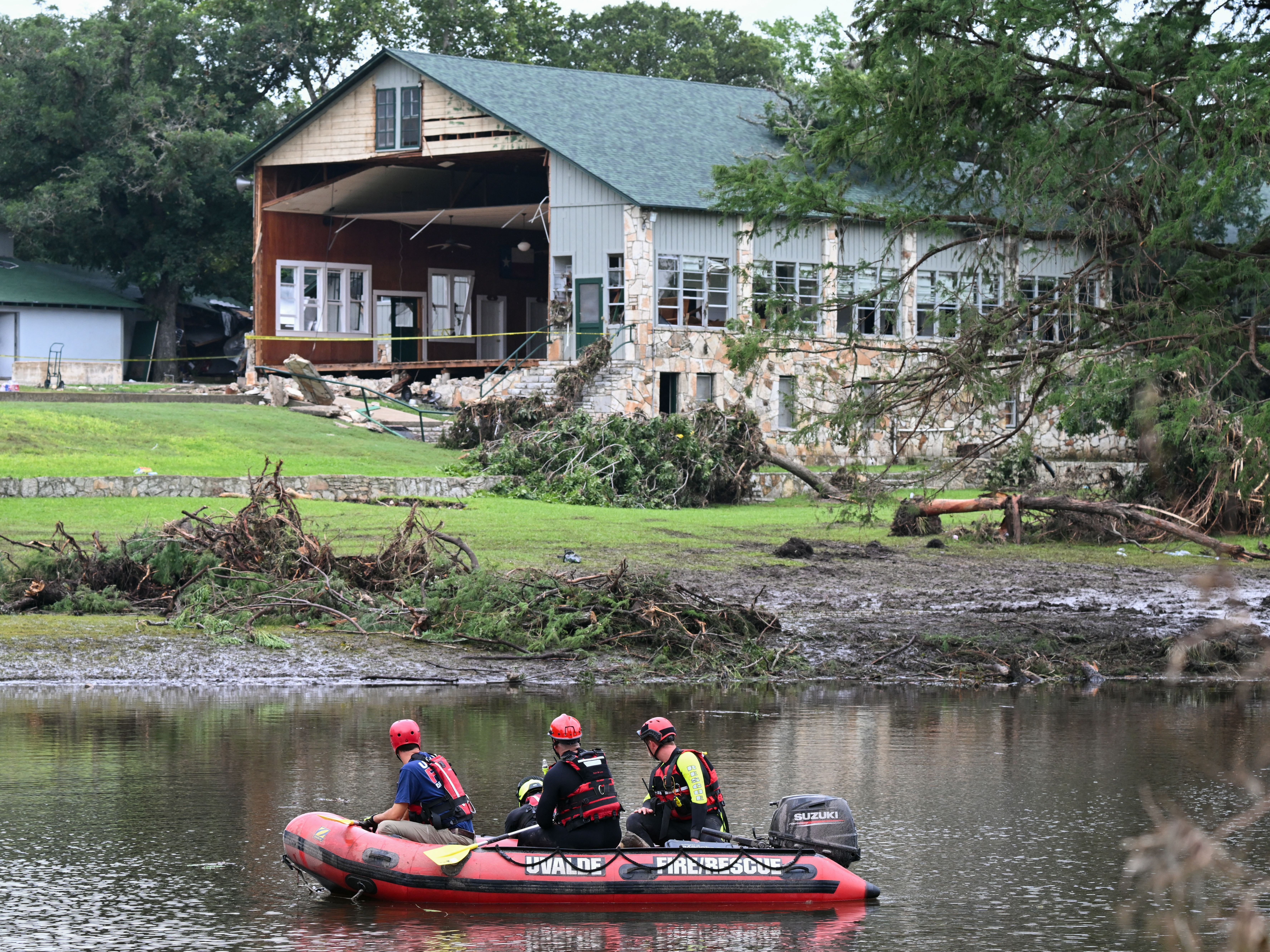 caption: A search and rescue team looks for people along the Guadalupe River near a damaged building at Camp Mystic. Federal regulators repeatedly granted appeals to remove Camp Mystic's buildings from government flood maps that showed they were in an area at high risk of dangerous flooding.
