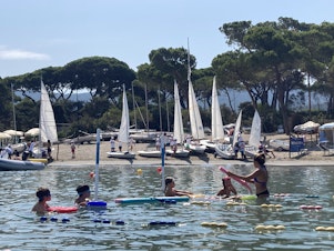 caption: Swimming and sailing classes are just a few of the sports on offer to families who vacation in Punta Ala. Families return year after year to give their children a break in nature and let them reunite with friends they only see in the summer.