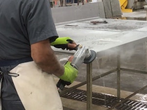 caption: This image, from a video produced by government safety researchers, shows a countertop worker using a machine with a spray of water that's intended to control dust.