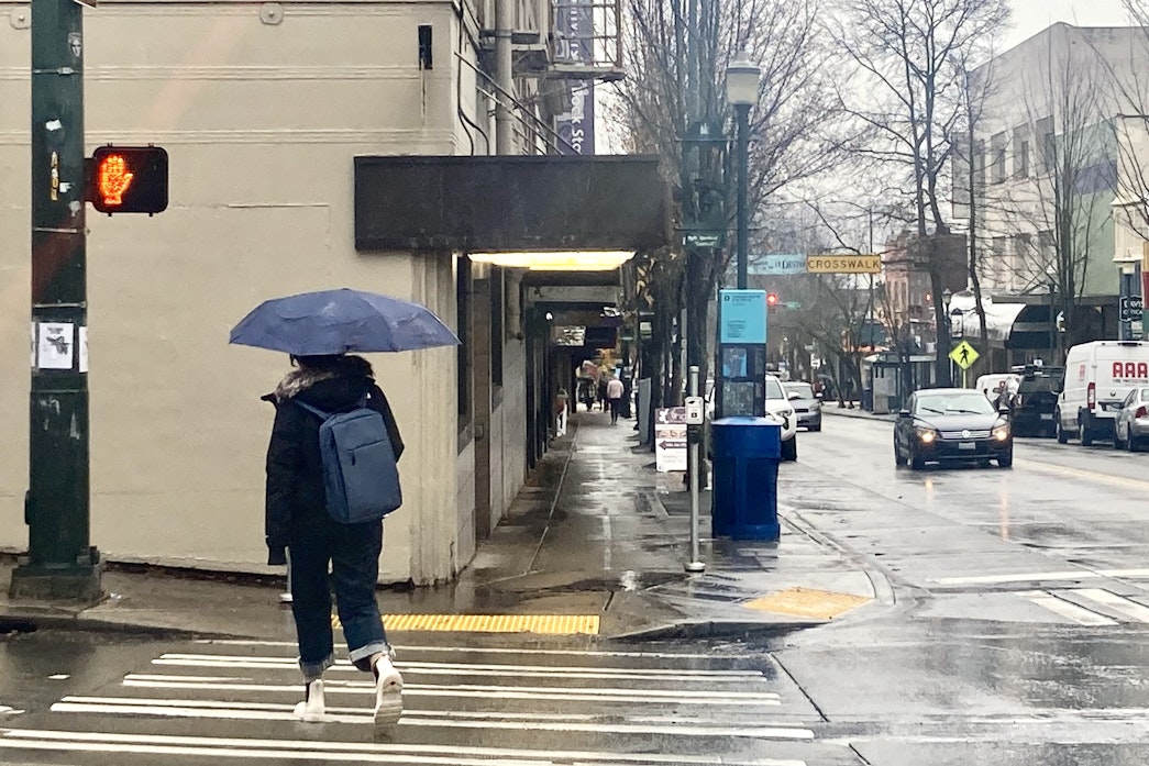 caption: A person with an umbrella walks down University Avenue as an atmospheric river drenches Seattle on Dec. 4, 2023.