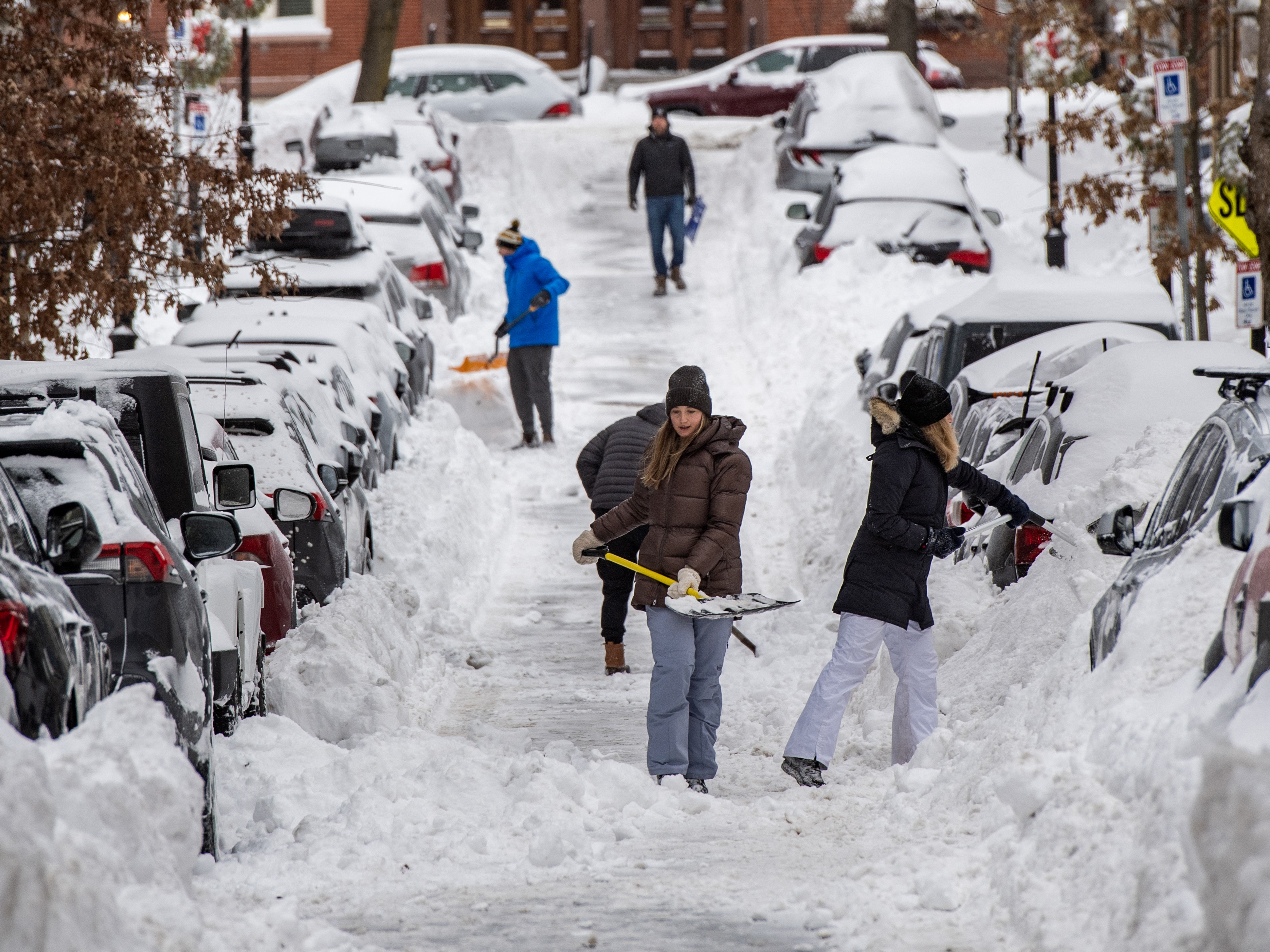 caption: People shovel snow along a residential street in Boston on Monday.
