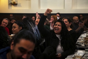 caption: Aretha Basu cheers during a gathering to celebrate the effort of those who worked to secure uncommitted delegates to send a message to President Biden, as initial results arrive for the presidential primary on Tuesday, March 12, 2024, at Tanoor in Seattle. 