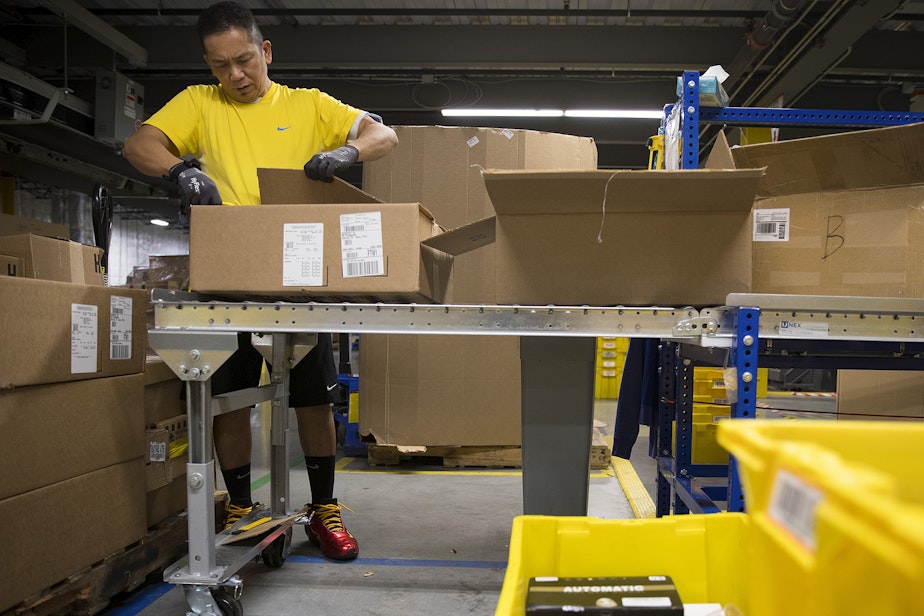 caption: Amazon employee Larry Rafols distributes items to different stations at an Amazon fulfillment center on Friday, November 3, 2017, in Kent.