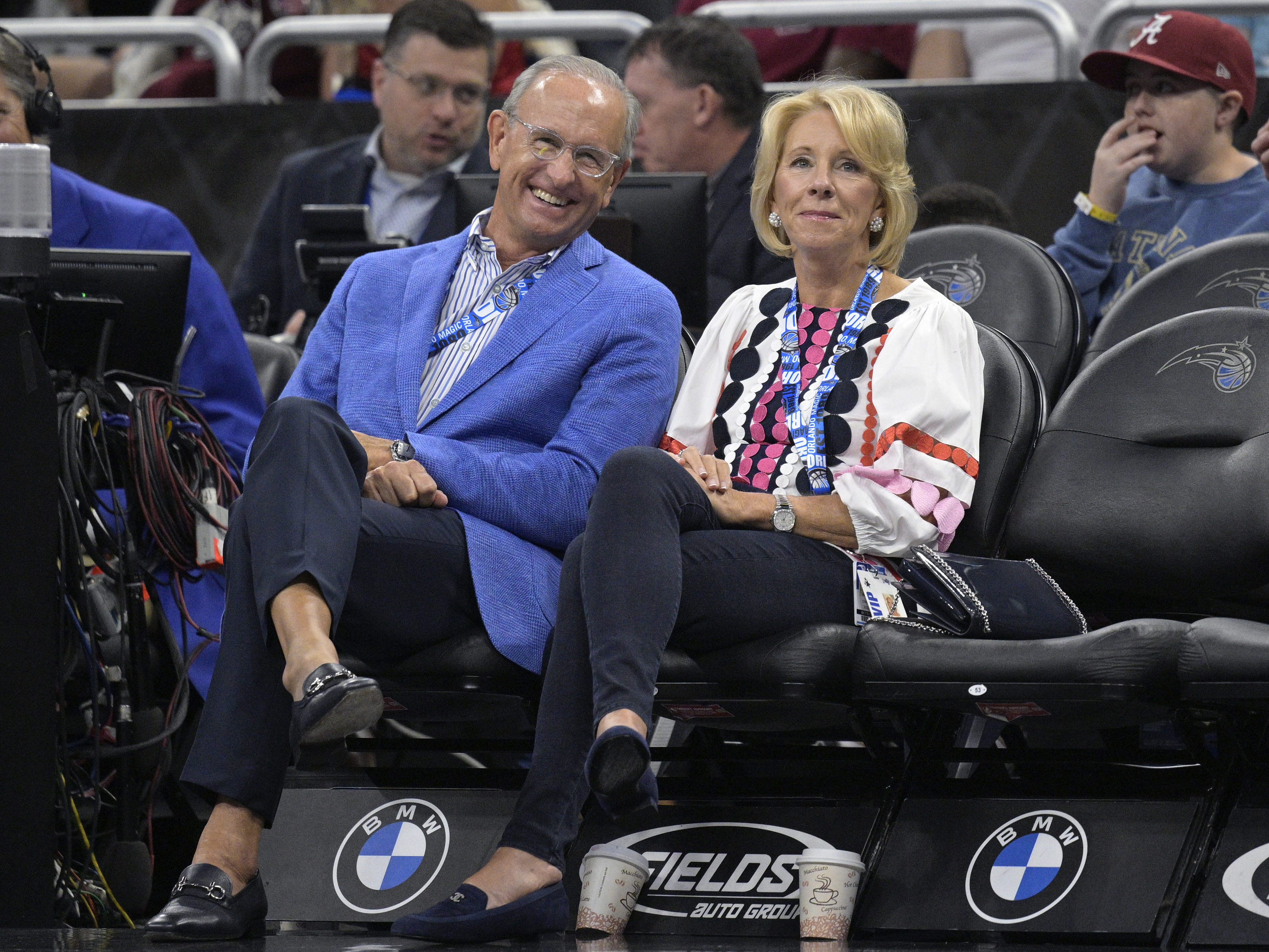 caption: Dick DeVos (left) and former Secretary of Education Betsy DeVos watch from courtside seats during a game between the Orlando Magic and the Brooklyn Nets on March 26 in Orlando, Fla. The Magic is owned by the DeVos family.