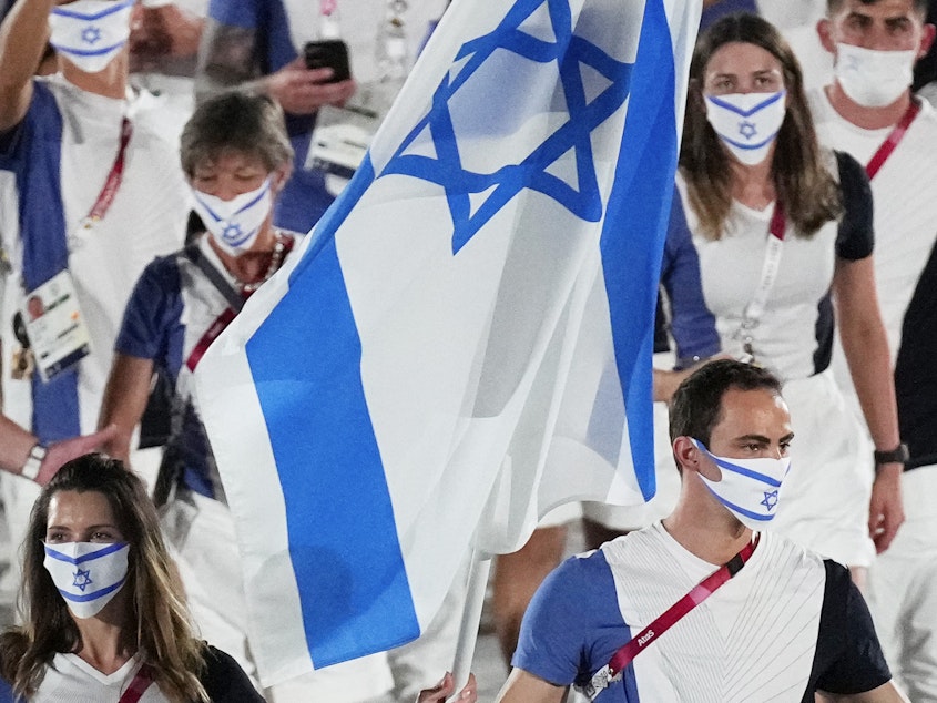 caption: Hanna Minenko and Yakov Toumarkin, of Israel, carry their country's flag during the opening ceremony in the Olympic Stadium at the 2020 Summer Olympics in Tokyo.