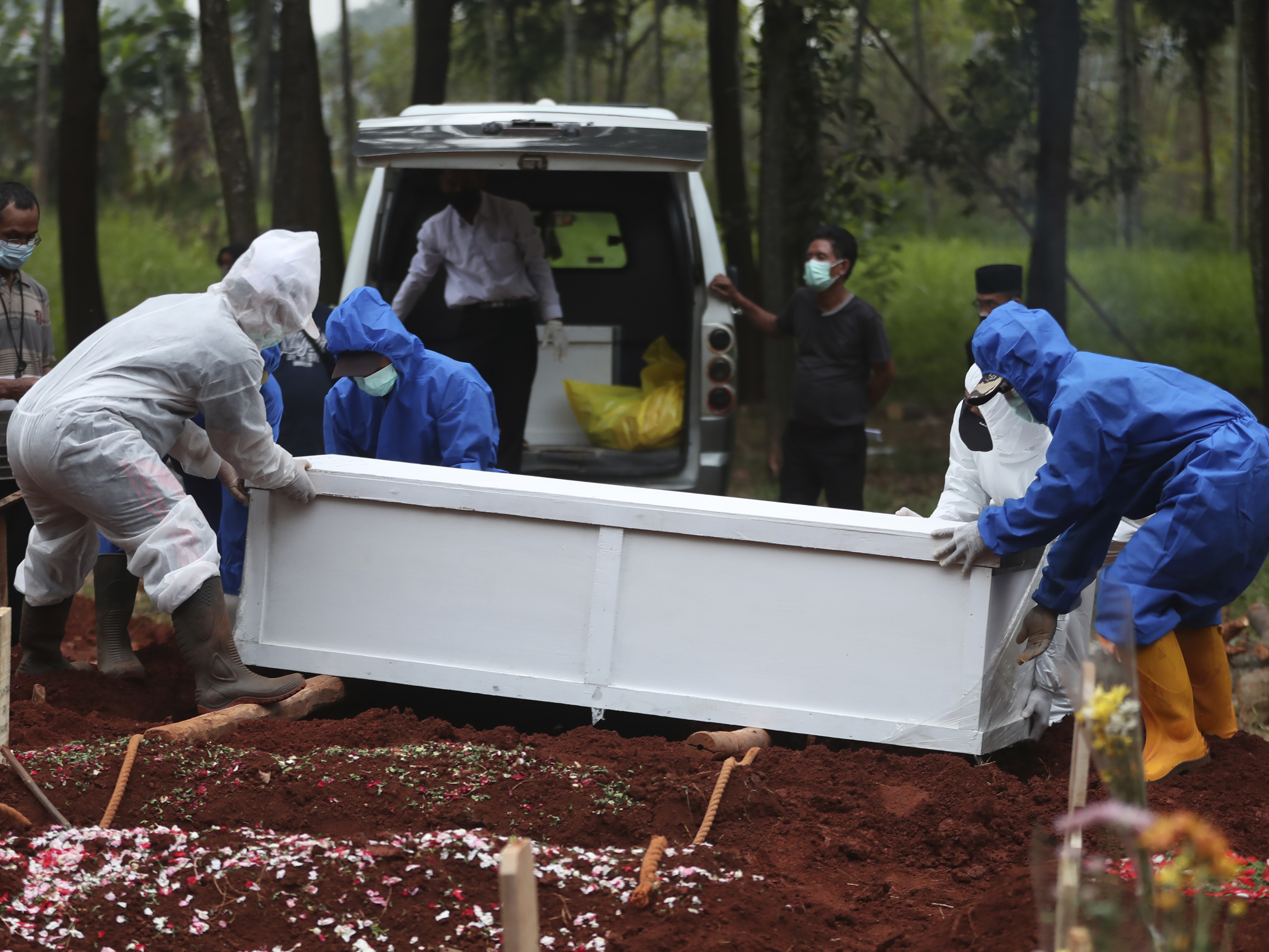 caption: Workers in protective suits carry a coffin containing the body of a COVID-19 victim to a grave for burial at the Cipenjo Cemetery in Bogor, West Java, Indonesia, Wednesday, July 14, 2021.