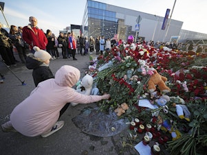caption: People lay flowers at a makeshift memorial in front of the Crocus City Hall outside Moscow, on Monday. There were calls Monday for harsh punishment for those behind the attack on the Russian concert hall that killed more than 130 people, as authorities combed the burnt-out ruins of the shopping and entertainment complex in search of more bodies.