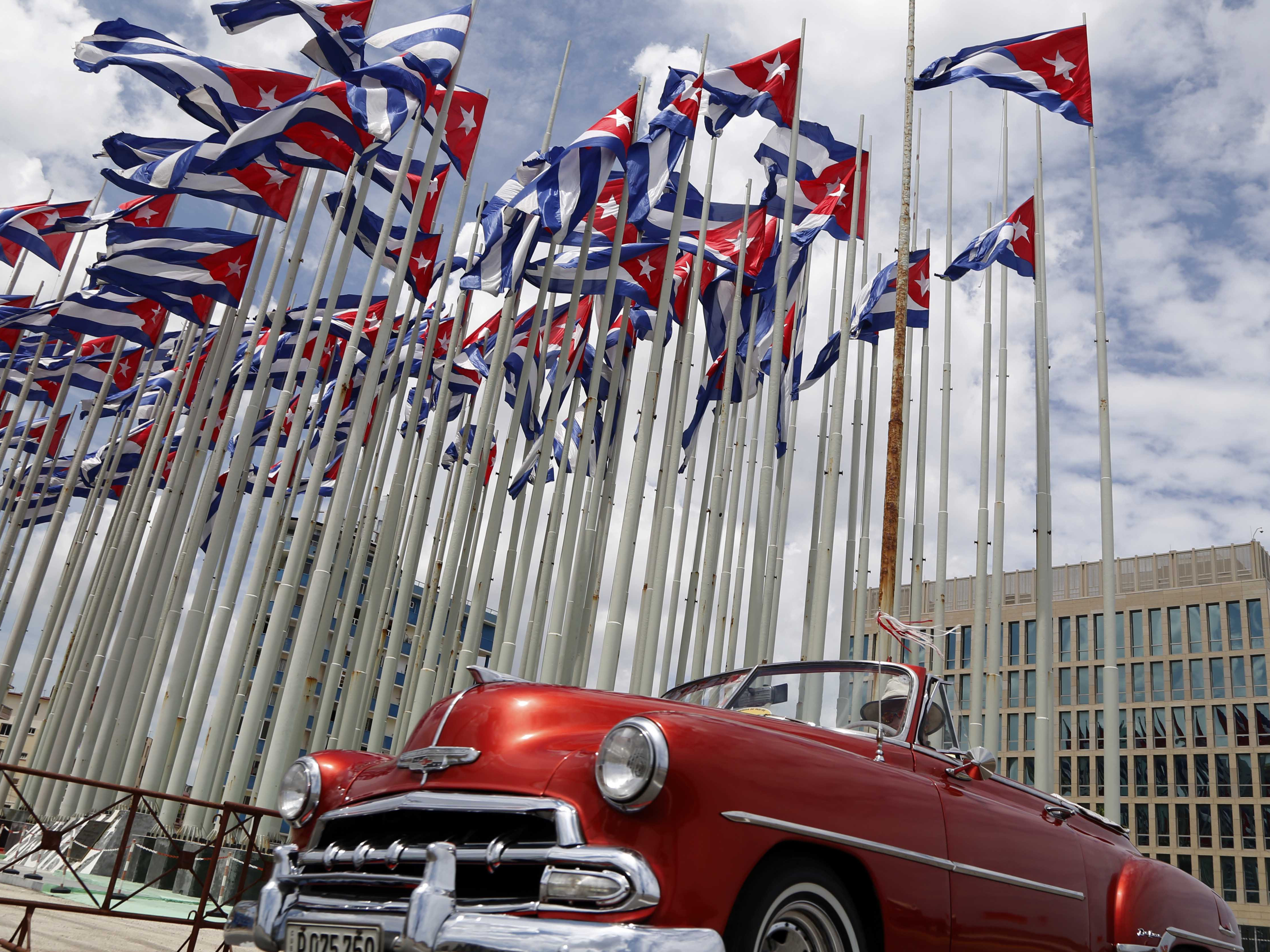 caption: A classic American convertible car passes beside the United States embassy as Cuban flags fly at the Anti-Imperialist Tribune, a massive stage on the Malecon seaside promenade in Havana, Cuba, July 26, 2015.