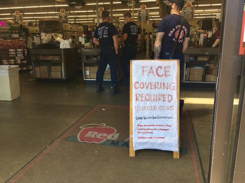 caption: A sign at the entrance of the Hilltop Red Apple Market asks customers to wear a mask. 