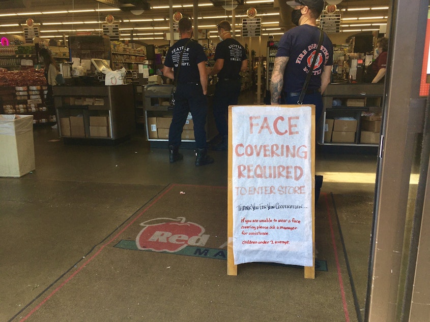 caption: A sign at the entrance of the Hilltop Red Apple Market asks customers to wear a mask.