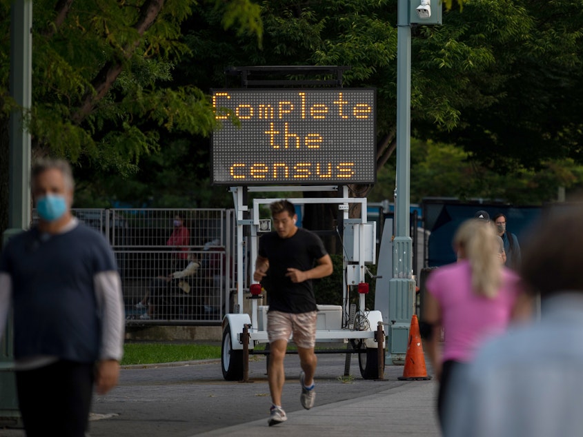 caption: People pass by a "Complete the census" sign along New York City's Hudson River Greenway in September 2020.