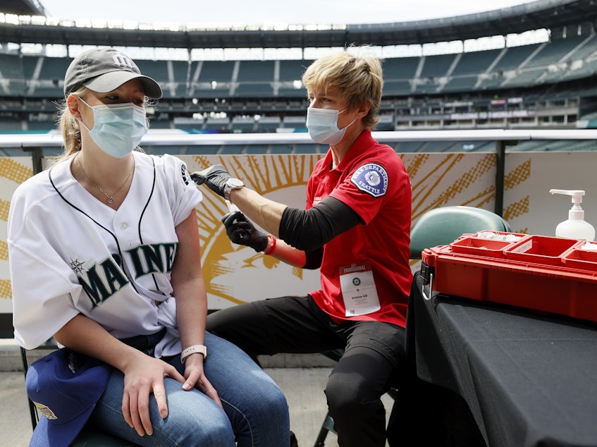 caption: Sydney Porter of Bellevue, Wash., receives her COVID-19 vaccination from Kristine Gill, with the Seattle Fire Department's Mobile Vaccination Teams, before the game between the Seattle Mariners and the Baltimore Orioles at T-Mobile Park on May 5 in Seattle. A late spring COVID-19 surge has filled hospitals in the metro areas around Seattle.
