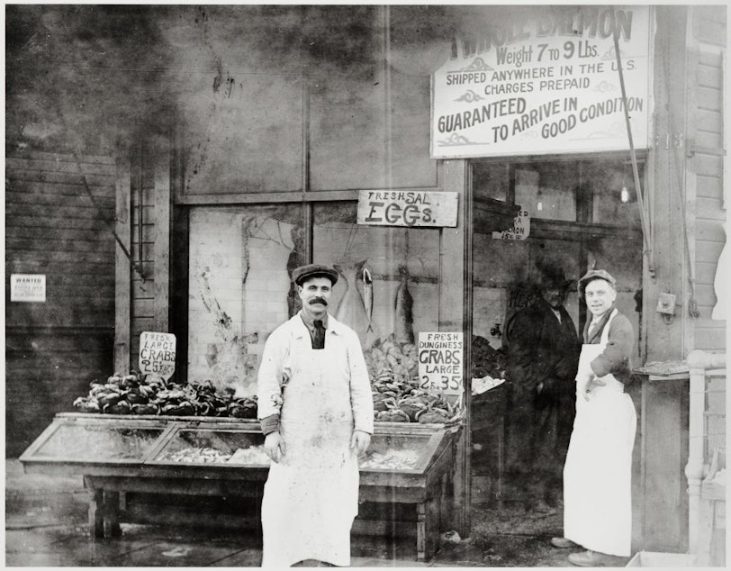 caption: Solomon Calvo (left) and Fred August in front of the Waterfront Fish and Oyster Co., Pike Place Market, Seattle, ca. 1918. Calvo was one of the original Sephardic migrants to Seattle. 