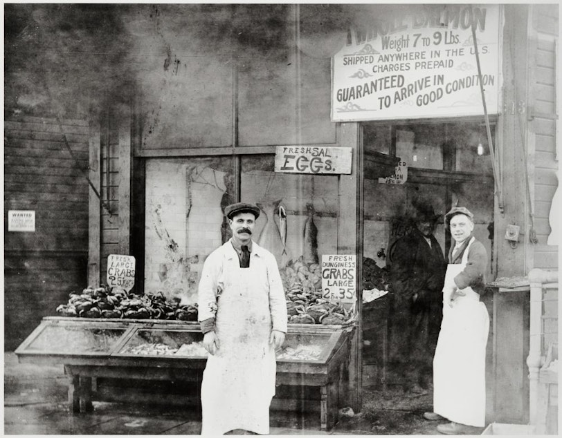 caption: Solomon Calvo (left) and Fred August in front of the Waterfront Fish and Oyster Co., Pike Place Market, Seattle, ca. 1918. Calvo was one of the original Sephardic migrants to Seattle.