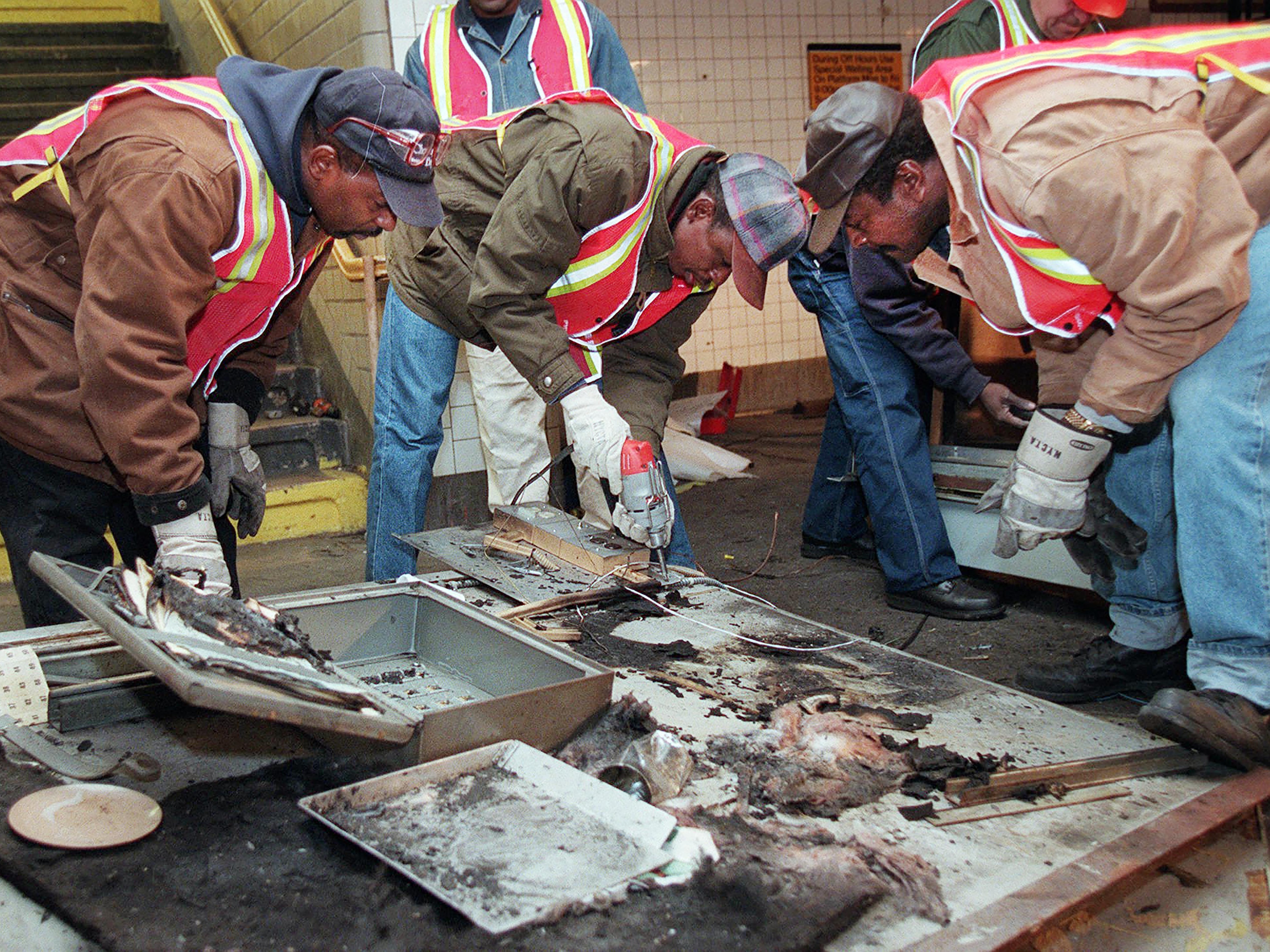 caption: Transit workers dismantle the charred inner wall of a token booth at the Kingston Avenue and Fulton Street subway station in the Bedford-Stuyvesant section of Brooklyn, on Nov. 26, 1995, after attackers sprayed a flammable liquid into the token booth and lit it on fire, according to police.