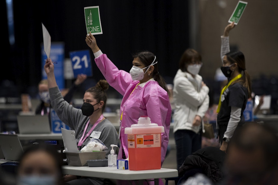 caption: Volunteer Dr. Aditi Agardwal, center in pink, raises a piece of paper indicating that she needs more vaccine on Saturday, March 13, 2021, at the new civilian-led mass Covid-19 vaccination site at Lumen Field Event Center in Seattle. 