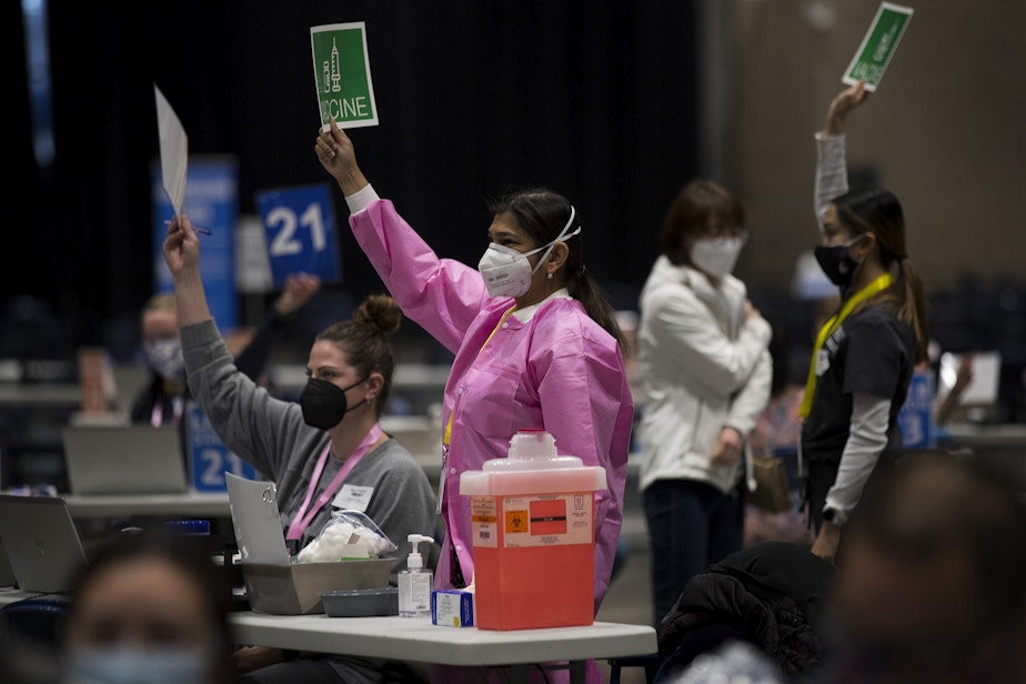 caption: Volunteer Dr. Aditi Agardwal, center in pink, raises a piece of paper indicating that she needs more vaccine on Saturday, March 13, 2021, at the new civilian-led mass Covid-19 vaccination site at Lumen Field Event Center in Seattle.