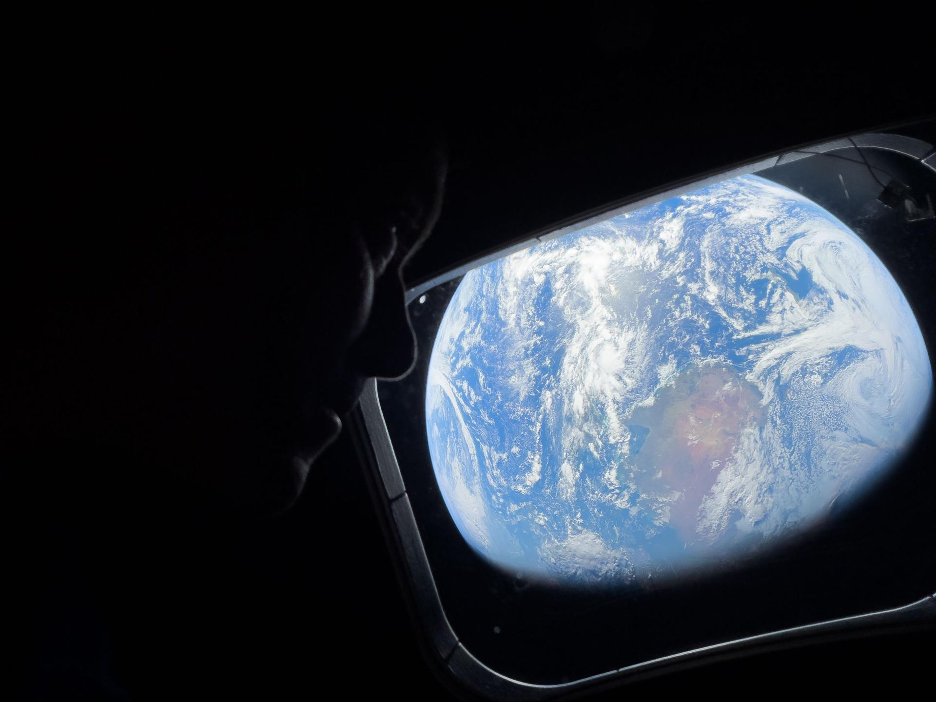 caption: NASA astronaut and Artemis II Commander Reid Wiseman looks at Earth through Orion's main cabin windows as the crew travels towards the moon. Wiseman and his three crewmates are set to return to Earth on Friday.