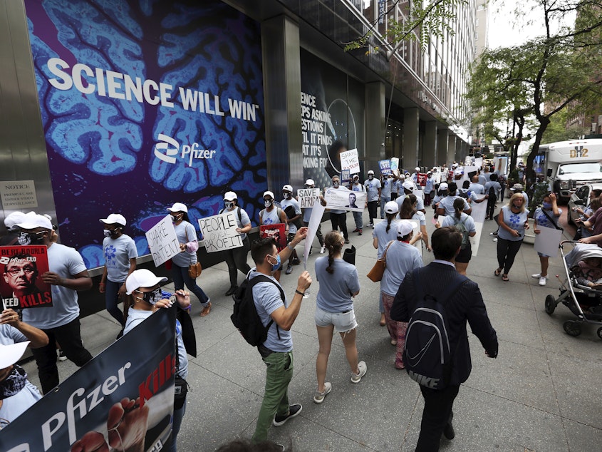 caption: Pfizer's agreement with a U.N. group to let other companies produce its new antiviral pill as a generic drug is meeting with a mixed reaction. In late summer, protesters at Pfizer's world headquarters in New York urged the drugmaker to broadly share the patent for its COVID-19 vaccine.