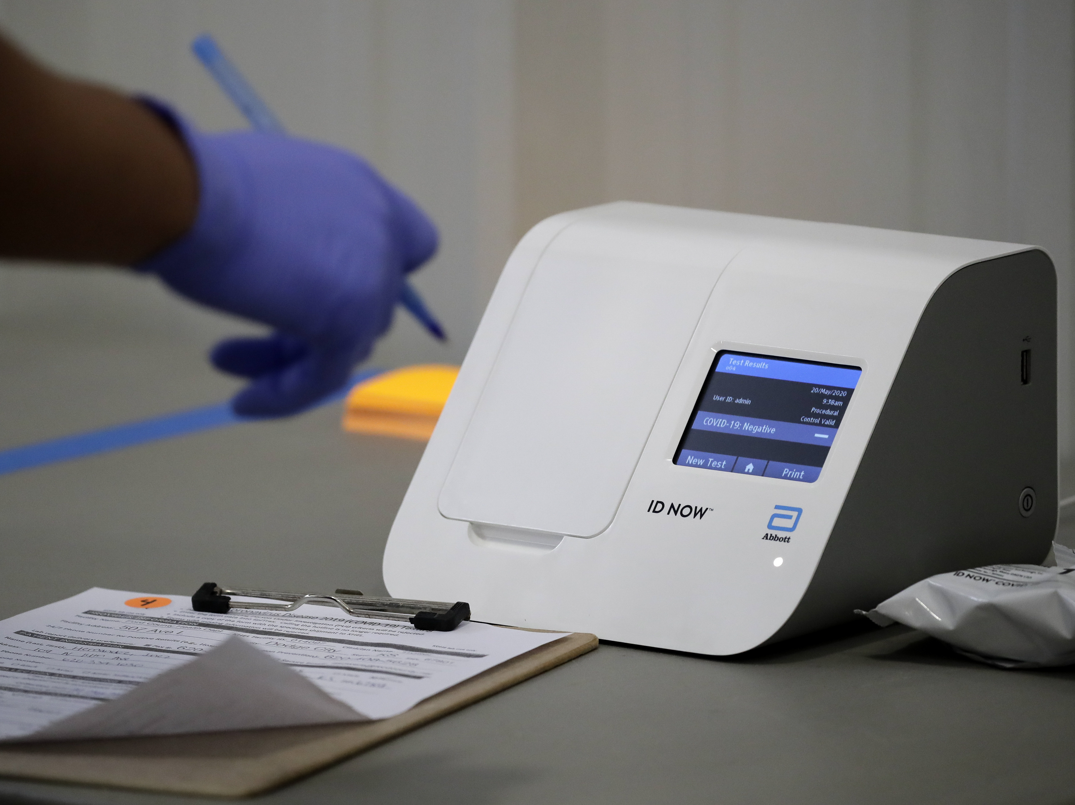 caption: Kansas National Guard member Roy Manns, from Topeka, Kan., writes down results as he runs samples through an Abbott COVID-19 testing machine at a drive-thru testing site on Wednesday in Dodge City, Kan.