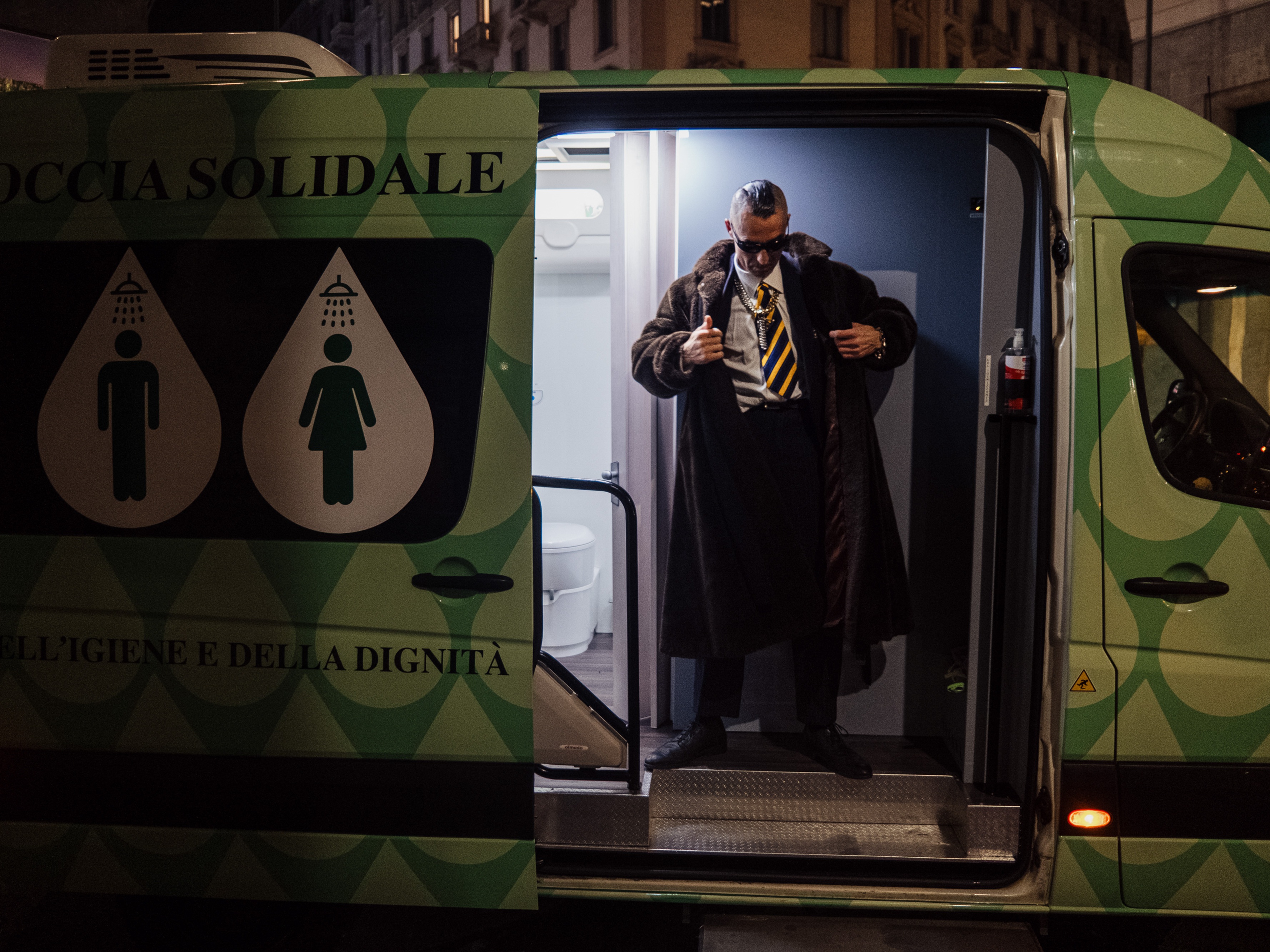 caption: This man is stepping out from a van that offers showers and bathroom facilities to the homeless. Known for his elegant garb, he is one of the 2,000 or so people who live on the streets in Milan, Italy — the number comes from a city survey. An Italian charity called Alatha sponsors the "solidarity shower" van.