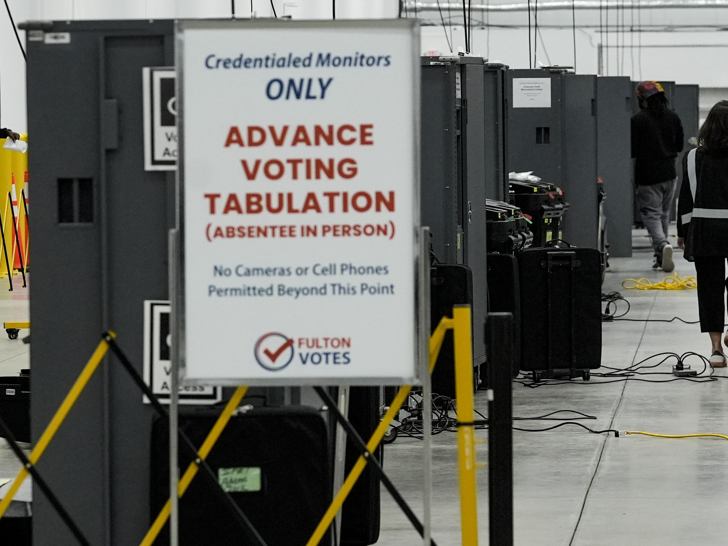 caption: An election worker walks near voting machines at the Fulton County Election Hub and Operation Center on Nov. 5, 2024.