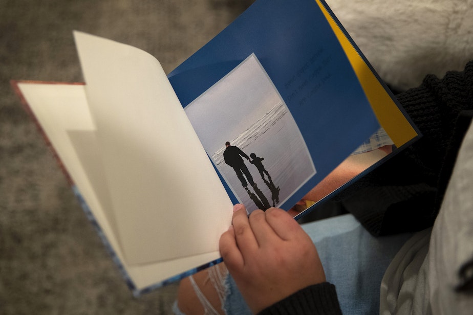 caption: Kaitlyn Mrsny, 13, flips through a book of images of her father, Kurt, on Thursday, December 9, 2022, at the Mrsny home in Puyallup. Here, Kurt holds hands with his son Cadence while walking on a beach.