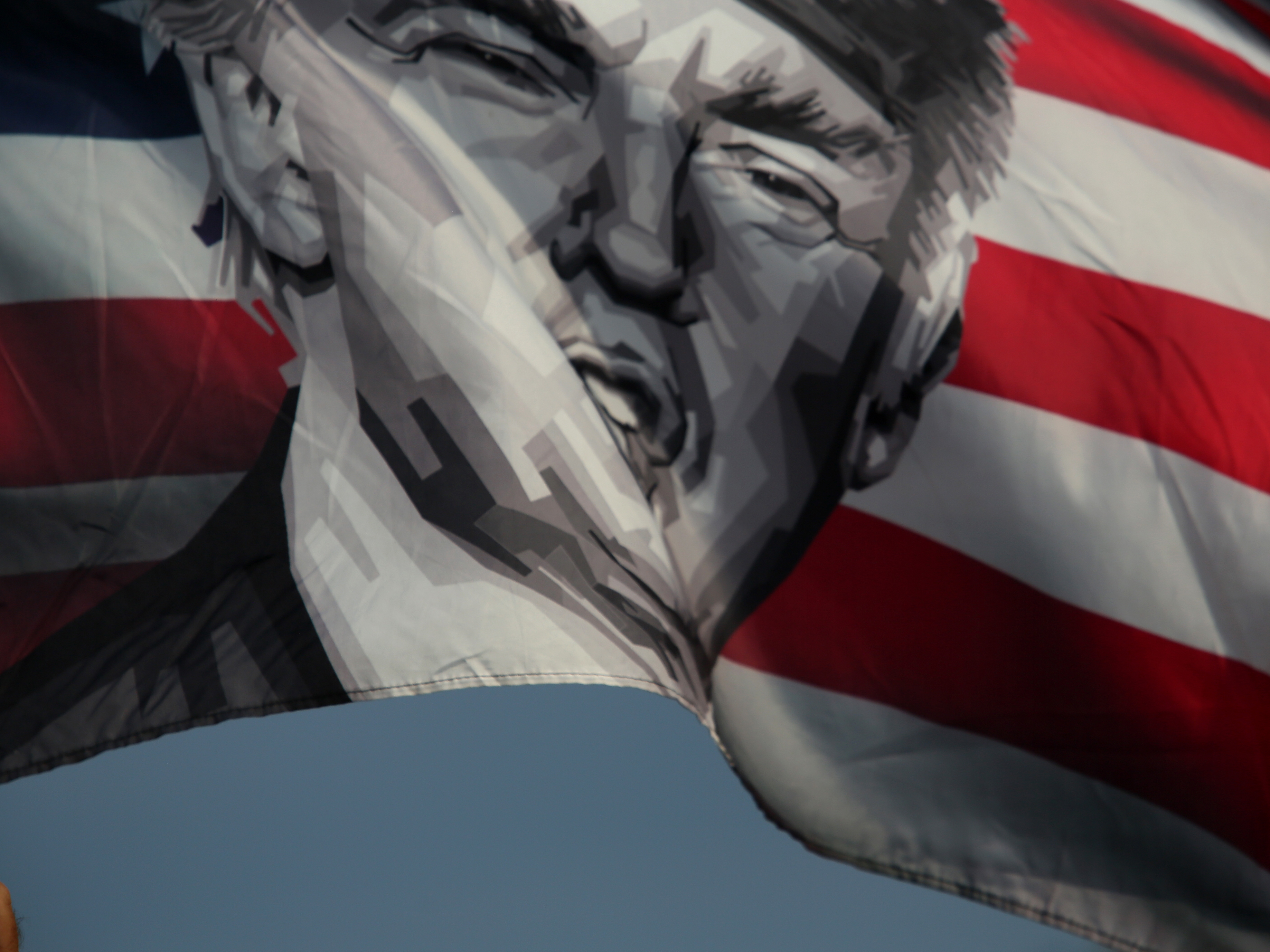 caption: A flag featuring Donald Trump waves amid a small group of his supporters near Mar-a-Lago in May 2024 in Palm Beach, Fla.