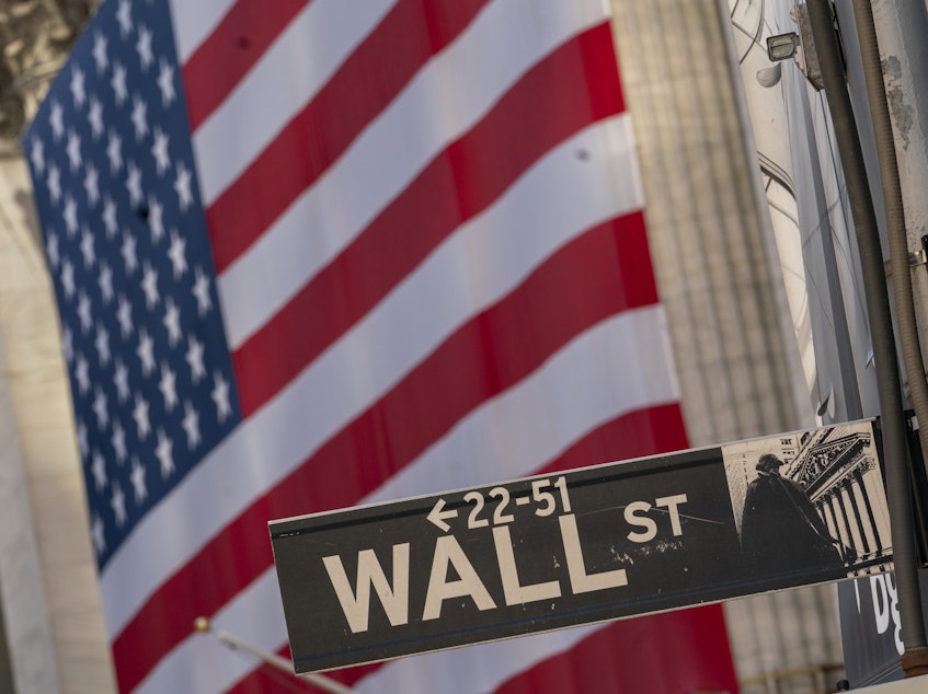caption: The Wall Street sign is shown framed by the American flag hanging on the New York Stock Exchange, on Sept. 21, 2020. Stocks posted their best weekly gain since April despite an uncertain election.