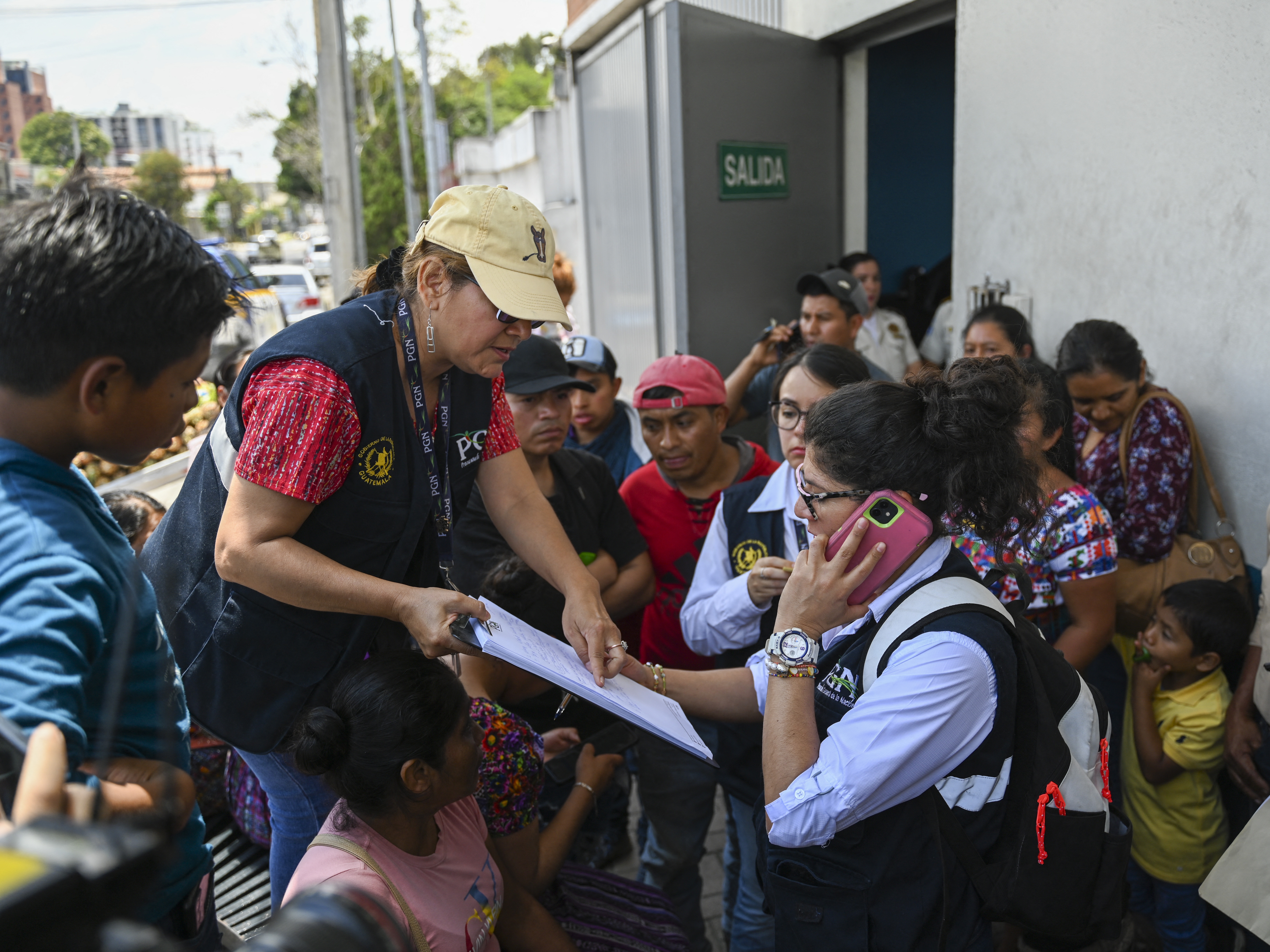 caption: Staffers of the Attorney General's Office take the data of relatives outside of the Returnee Reception Center while waiting for the arrival of minors intended to be deported from the United States, at the Guatemalan Air Force Base in Guatemala City on Aug. 31.