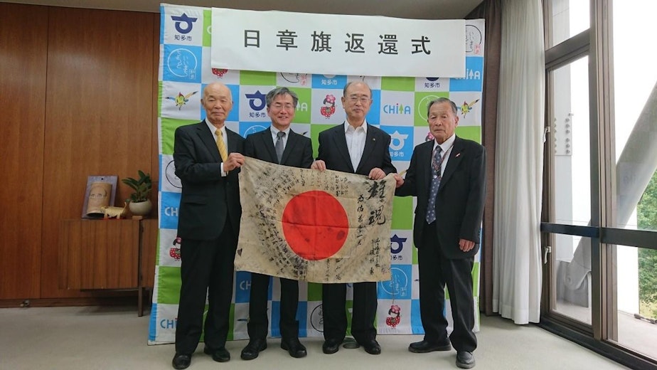 caption: The WWII flag submitted by Greg Murphy of Portland was traced back to a fallen Japanese soldier who carried it into battle in 1944. The mayor of Chita City, Japan, second from right, hosted a ceremony in 2019 where a nephew of the soldier, second from left, accepted the returned flag.