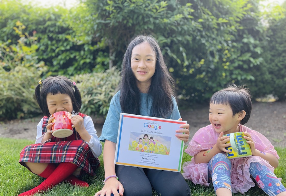 caption: Bellevue's Rebecca Wu holds her winning illustration for the national Doodle for Google competition, along with her two sisters. 