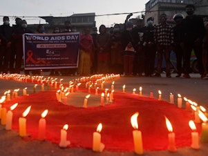 caption: Volunteers stand after lighting candles in the shape of a red ribbon during an awareness event ahead of World AIDS Day in Kathmandu on Tuesday.