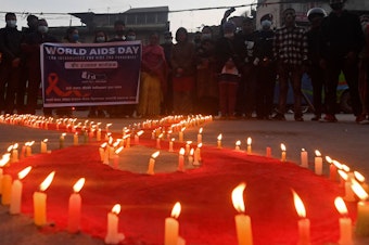 caption: Volunteers stand after lighting candles in the shape of a red ribbon during an awareness event ahead of World AIDS Day in Kathmandu on Tuesday.