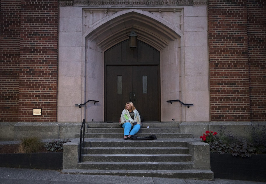 caption: Milee Ballweg, 20, sits on the steps of a University District church where she sleeps just after 5:00 a.m. on Wednesday, July 11, 2018, in Seattle.