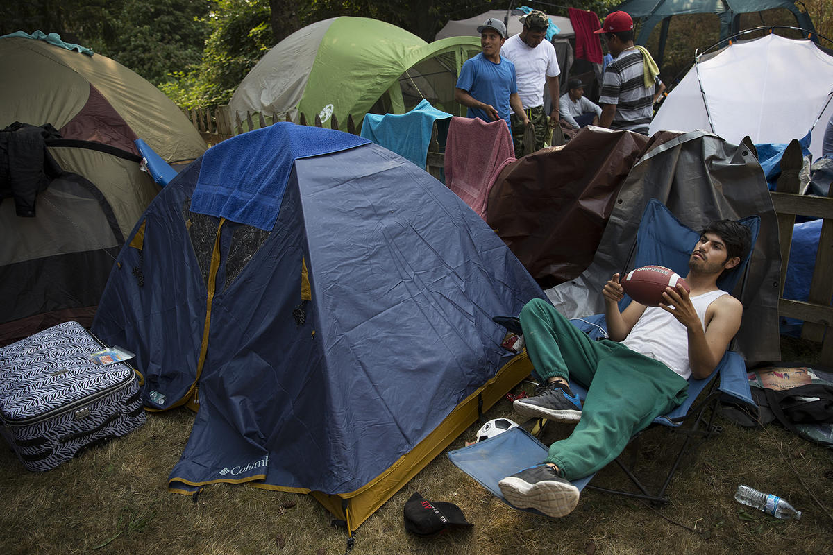 caption: Gerardo Rojas Olivarez plays with a football while passing the time on Wednesday, August 8, 2017, at a home in Sumas where farmworkers stayed in tents after being fired for insubordination from Sarbanand Farms.
