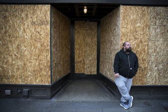 caption: Andy Aronis, Assistant General Manager of King's Hardware, smokes a cigarette outside of the boarded up bar and restaurant on Tuesday, March 17, 2020, on Ballard Avenue Northwest in Seattle. "I always felt good working in the bar industry because it's recession proof," said Aronis, who planned to file for unemployment. "The only thing you don't consider working in this industry is if there is a medical pandemic and then we are in the worst industry you could be in." 