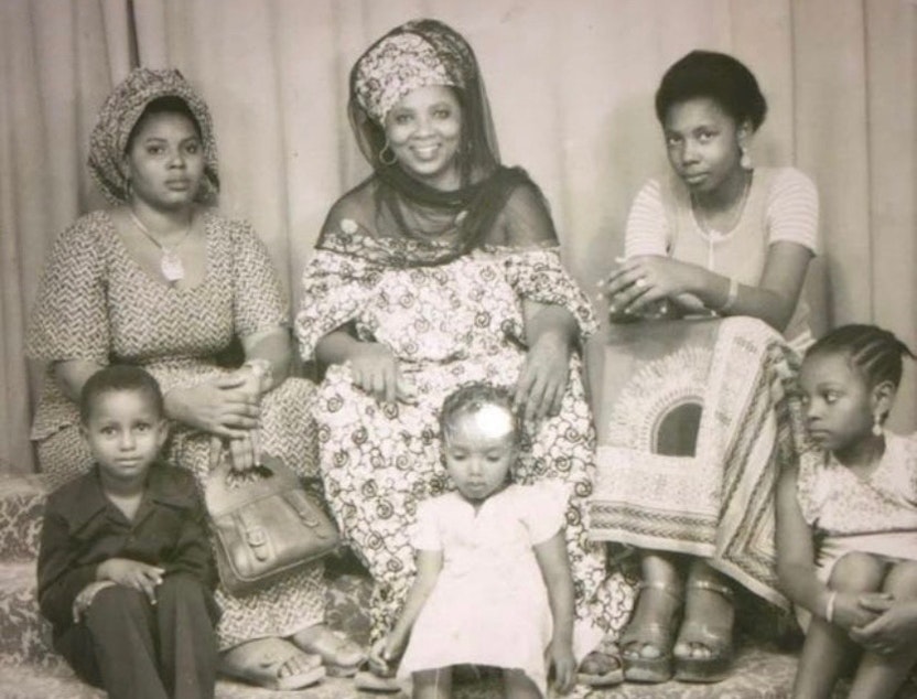 caption: Family portrait taken in Niger in 1978. Leila M’baye's great-grandma, Hadjia Mecca, smiles in the center of the top row. Hadjia's two daughters sit on either side of her, and her three grandchildren sit in the front row. Leila’s mom, Aissata M’baye, is on the lower right.