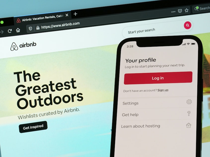 caption: The login page for Airbnb's iPhone app is seen in front of a computer displaying Airbnb's website, Saturday, May 8, 2021, in Washington.