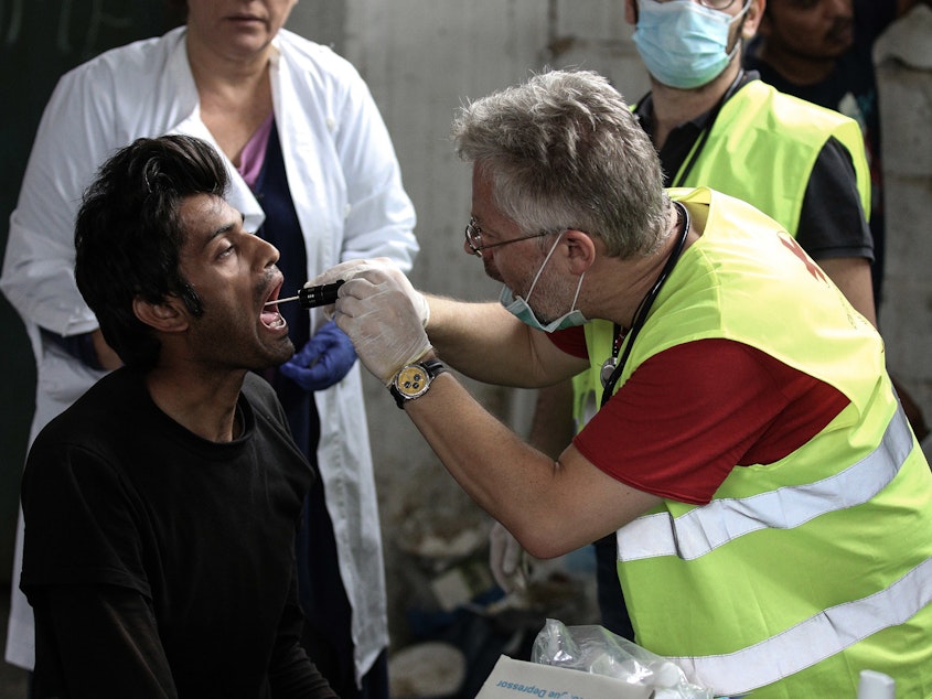 caption: A migrant receives medical attention at a former paper factory in Greece that has been turned into a makeshift camp.