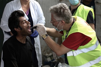 caption: A migrant receives medical attention at a former paper factory in Greece that has been turned into a makeshift camp.