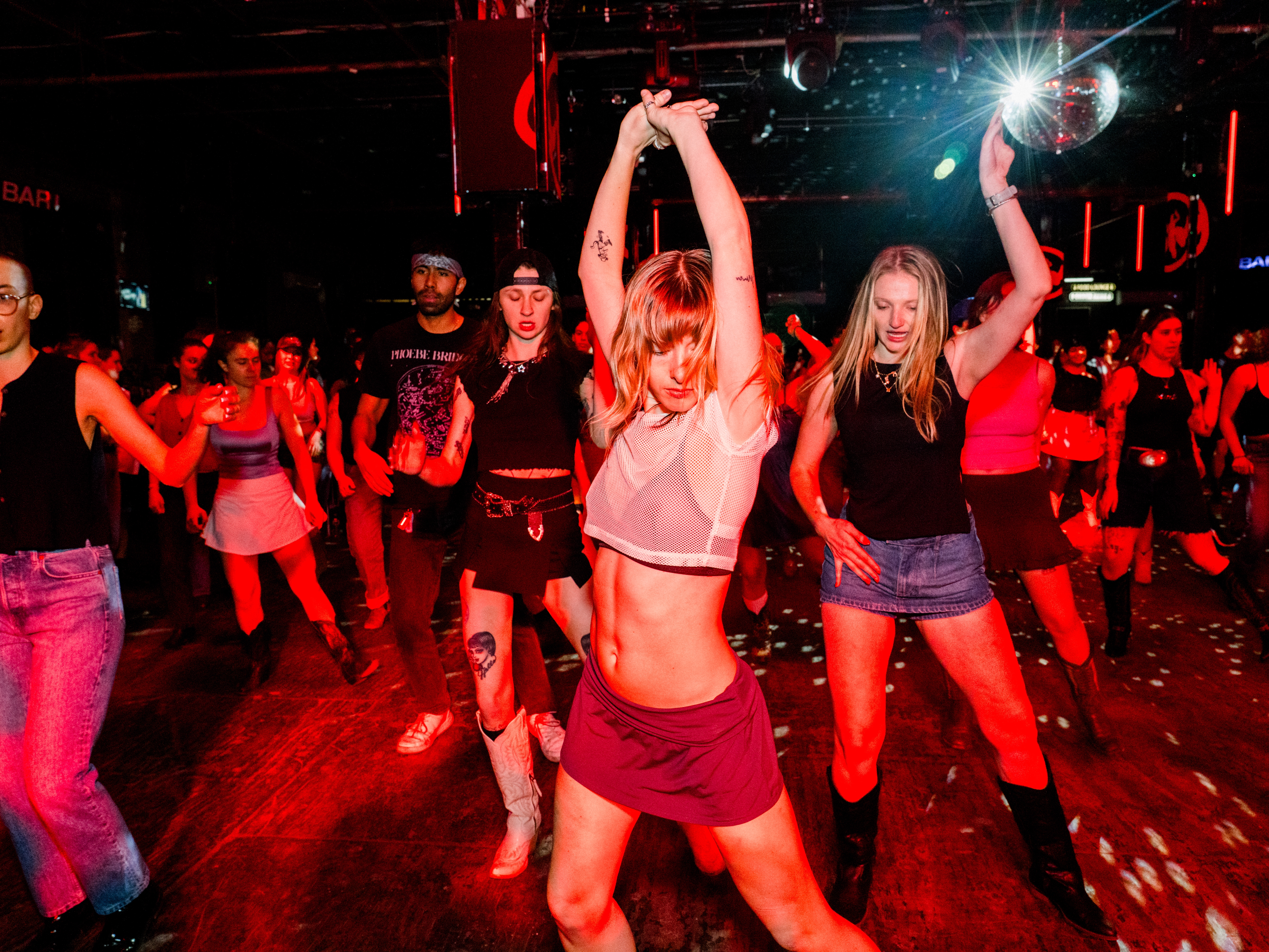 caption: Kitty Horblit (left), Karli Manship (center) and Hannah Bruns (right) dance at Stud Country, a national queer line dancing event, on March 25, 2025, in Brooklyn, N.Y.