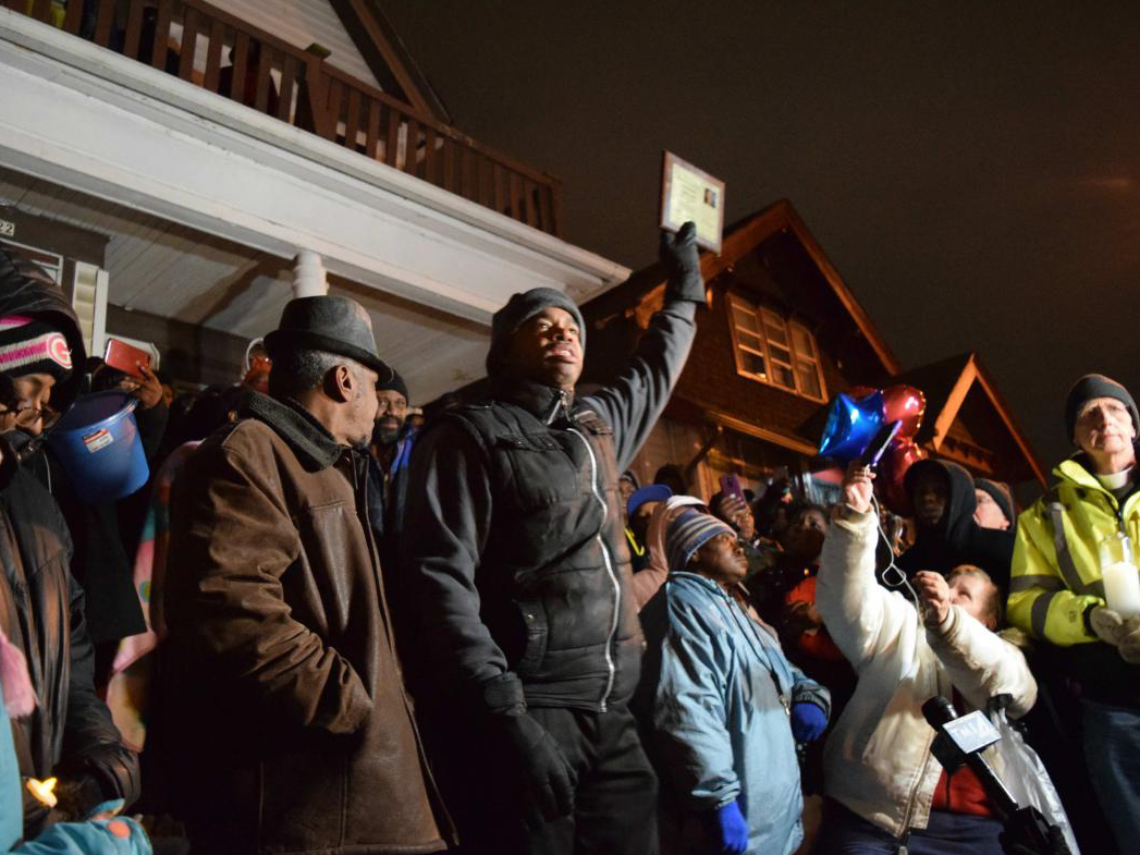 caption: Milwaukee community organizer Tracey Dent (center) holds up a third place award that Sandra Parks won at a vigil on Tuesday.