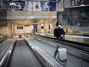 caption: A woman wearing a medical mask rides an escalator at Milan Central train station on Sunday after Italy's government locked down much of the country in an effort to stanch the spread of the coronavirus.